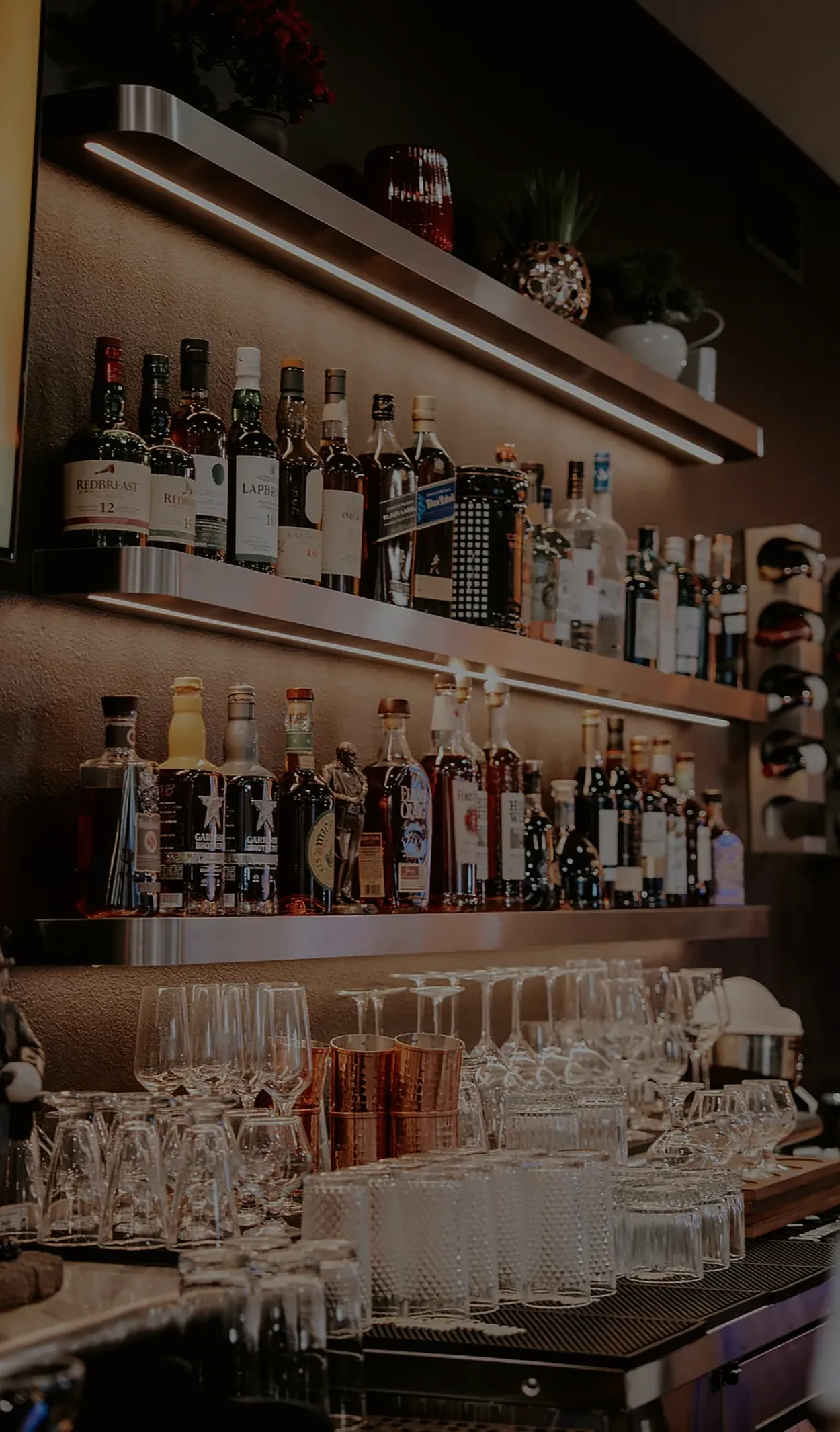 Shelves of wine and spirits behind the bar, glasses lined up below